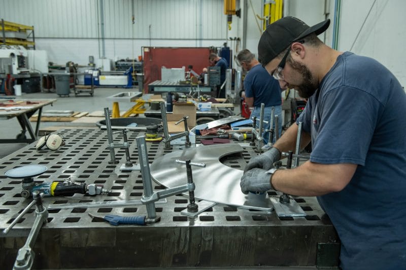 Fabricator forming and fitting curved stainless panel prior to final welding.
